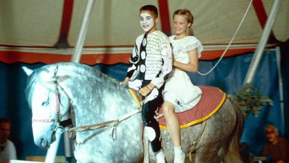 Rafael als Harlekin und Natascha reiten im Zirkuszelt auf einem weißen Pony © NDR 