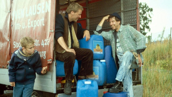 Fiete versteckt sich an der Seite eines LKWs auf dem zwei Männer Kamnister verladen © NDR 