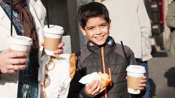 Emilio Sanmarino mit einem Croissant und einem ToGo-Becher in der Hand. © NDR Foto: Claudia Timmann