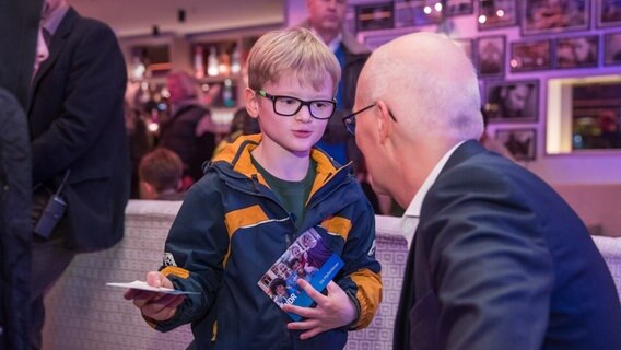 Kleiner Junge hält Pfefferkörner-Autogrammkarte in der Hand und unterhält sich mit dem Bürgermeister © NDR Foto: Axel Herzig