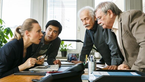 Vicky Adam (Katja Danowski, l.) und Hui Ko (Aaron Le, 2.v.l.) trauen ihren Augen kaum, als sie die Fahndungsbilder in der Zeitung sehen. Günter (Wolfgang Winkler, r.) und Edwin (Tilo Prückner, 2.v.r.) sollen einen Antiquitätenhänder überfallen haben? © NDR/ARD/Kai Schulz 