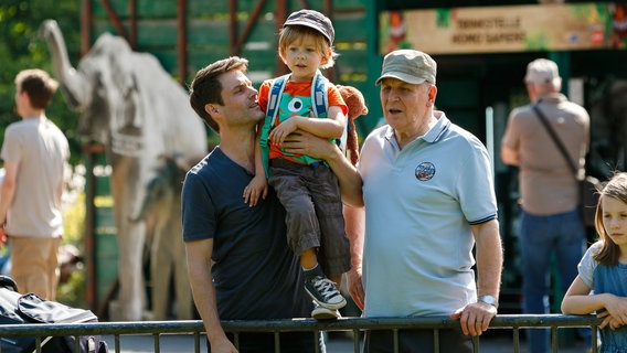 Finn (Florian Thürnagel, M.) besucht mit Papa Thomas (Sebastian Schlemmer, l.) und Opa Georg (Stefan Viering, r.) den Zoo (mit Komparsen). © NDR/ARD/Kai Schulz 
