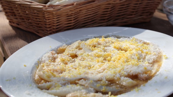 Weißer Spargel mit Parmesan und Zitronenabrieb auf einem Teller serviert. © NDR Foto: Florian Kruck