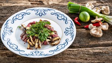 Flanksteak mit Rucola und Shiitake-Pilzen auf einem Teller angerichtet. © NDR Foto: Frank von Wieding