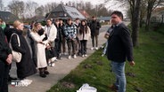 Glückstädter Schüler stehen an einer Straße und hören einem Mann zu bei der Spurensuche des NS-Todesmarschs. © NDR 