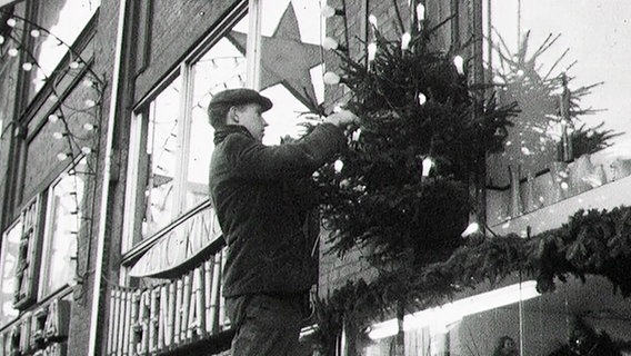 Ein Mann befestigt einen Weihnachtsbaum an einem Schaufenster. © NDR Foto: NDR