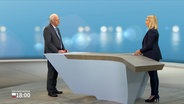 Reinhard Sager, Präsident Deutscher Landkreistag, steht an einem Tisch im Fernsehstudio gegenüber der Moderatorin Alexandra Bauer. © NDR 