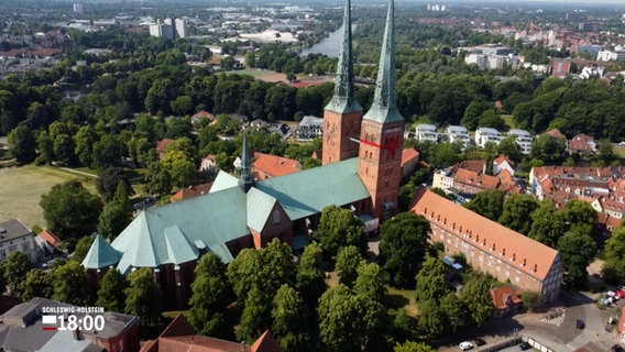 Eine Luftaufnahme zeigt den Lübecker Dom, einer der Türme ist mit einer großen roten Schleife verziert. © NDR Foto: NDR Screenshots