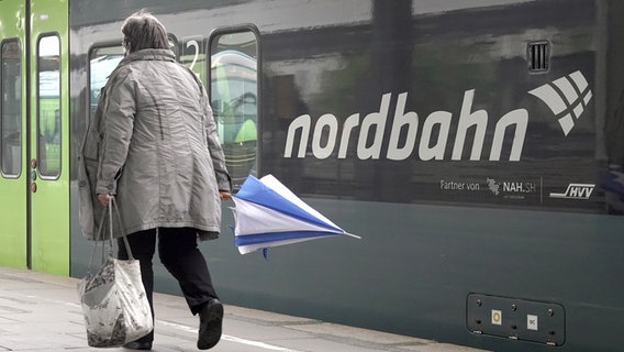 Eine Frau mit Regenschirm geht an einem Zug der nordbahn entlang, der im Bahnhof steht. © picture alliance/Bodo Marks Foto: Bodo Marks