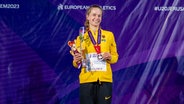 Adia Budde steht mit einer Silbermedaille und einer Trophäe auf einer Bühne und lächelt in die Kamera. © IMAGO / Beautiful Sports 