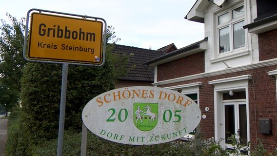 Neben dem Ortsschild des Dorfs "Gribbohm" im Kreis Steinburg steht ein Schild, auf dem "Schönes Dorf mit Zukunft 2005" steht. © NDR 