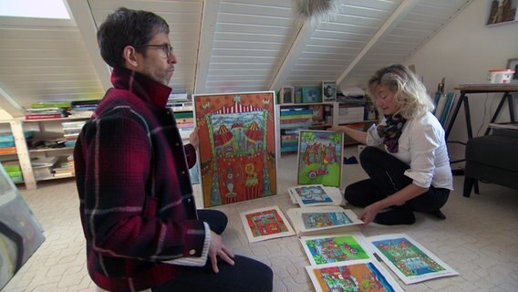 Sonja Mengkowski zeigt mit ihrem Mann in ihrem Atelier ihre gemalten Bilder. © NDR / SH Magazin Foto: Screenshot