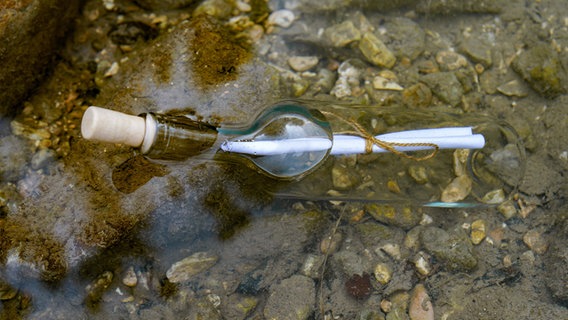 Eine Flaschenpost im Wasser schwimmend auf den Felsen am Meeresstrand. © IMAGO / imagebroker Foto: joseantona