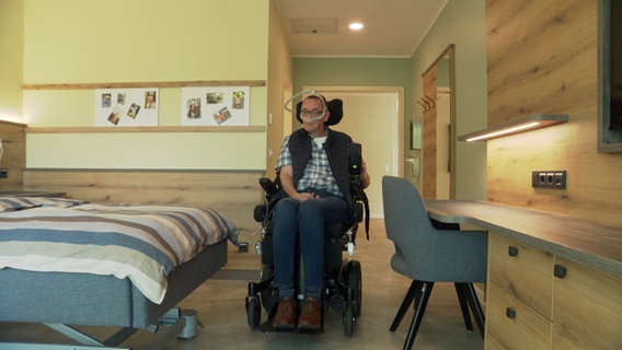 Ein Mann in einem Rollstuhl fährt in ein Zimmer eines Hospizes. © NDR Foto: NDR Screenshots