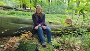 Pilzfachfrau Dagmar Detloff-Scheff sitzt im Wald auf einem ligenden Baumstamm, in der Hand einen kleinen Pilz. © NDR Foto: Dr. Andrea Ring