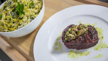 Auf einem Teller liegt ein gegrilltes Rumpsteak angerichtet und daneben steht eine Schüssel mit Fusilli in Zitronensahne. © NDR 