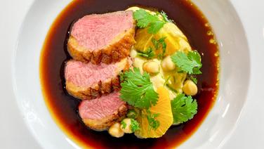 Crispy duck breast with chickpea puree and orange salad on a plate.  © NDR 