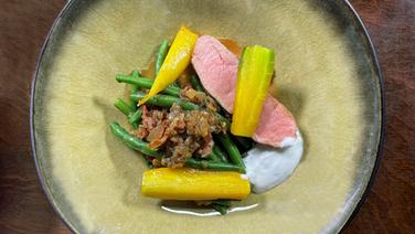 On a plate is pink roasted saddle with beans and carrots.  © NDR 