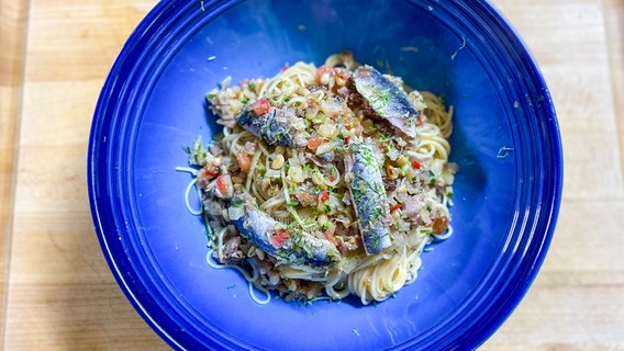 Spaghetti mit Sardinen und Estragon auf einem blauen Teller angerichtet. © NDR 