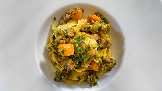 Tagliatelle mit Salsiccia, Kürbis und Parmesan auf einem Teller angerichtet. © NDR 