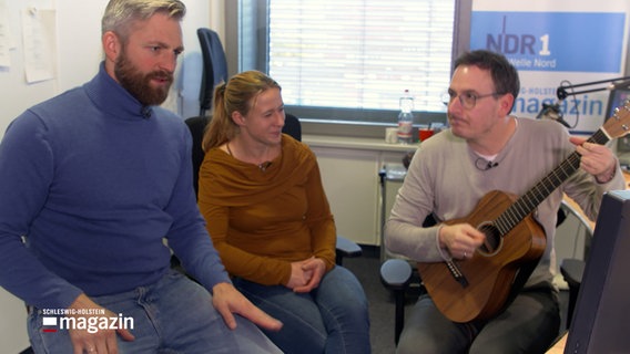 Phillip Jeß sitzt im Sendestudio der NDR 1 Welle Nord mit den Moderatoren Mandy Schmidt und Horst Hof. © NDR 