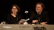 Autoren Mareike Krügel und Jan Christophersen sitzen an einem Tisch auf einer Bühne bei einer Lesung. © NDR 