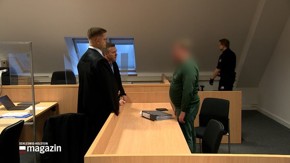 Ein Angeklagter unterhält sich mit seinem Verteidiger in einem Gerichtssaal. © NDR 