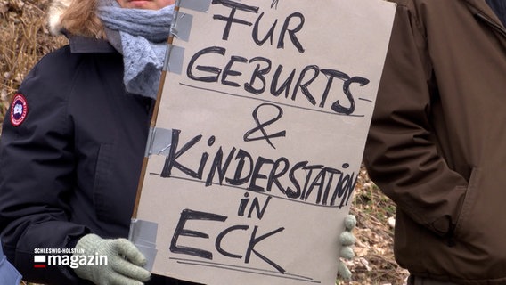 Eine Frau hält ein selbst gemachtes Schild mit dem Schriftzug "Für Geburts&Kinderstation in Eck" bei einer Protestaktion auf dem Geländer der Imland-Klinik in Eckernförde. © NDR 
