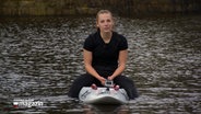 Rettungssprotlerin Janka Krohn sitzt auf einem Surfbrett in einem Gewässer. © NDR 