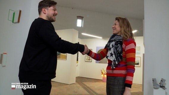 Ein Mann und eine Frau begrüßen einander mit einem Handschlag bei einer Kunstausstellun auf Wittkielhof in Stoltebüll. © NDR 