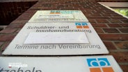Weiße Schilder hängen an der Wand eines Gebäudes. "Schuldner- und Insolvenzberatung Termine nach Vereinbarung" steht auf dem Schild in der Mitte. © NDR 