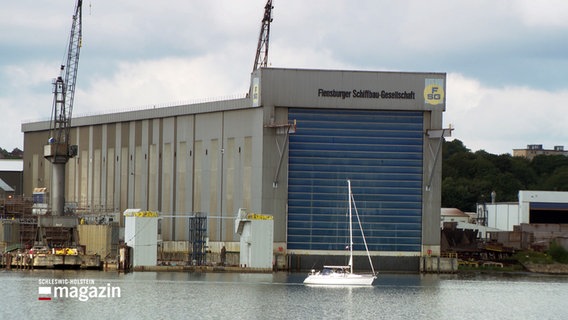 Ein weißes Segelboot fährt an der Halle der Flensburger Schiffbau Gesellschaft vorbei. © NDR 