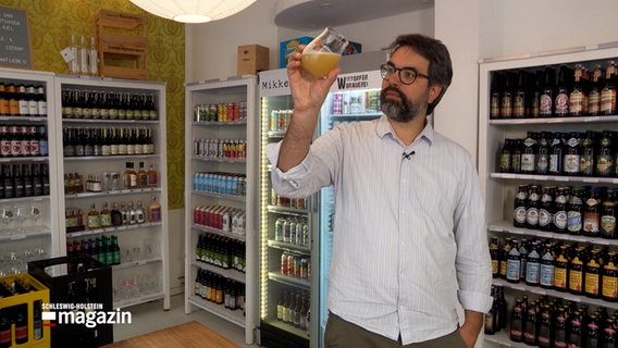 Lars Müller, der ehemalige Gründer von "Brewcomer" steht in einem Craftbeer-Laden und hält ein Glas mit Craftbeer in der Hand. © NDR 