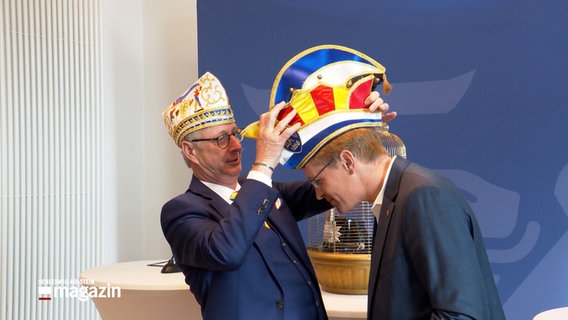Ministerpräsident Daniel Günther (CDU, r.) bekommt von Wolfgang Hyrenbach, Präsident Aachener Karnevalsverein eine bunter Mütze aufgesetzt. © NDR 