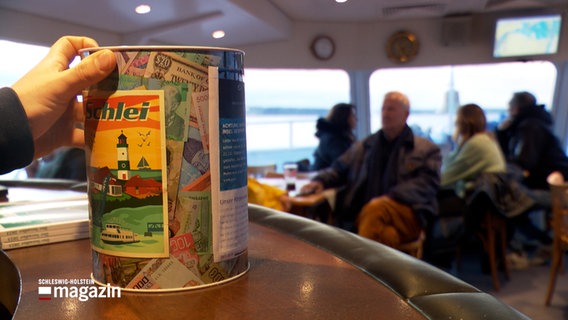Eine Spardose steht auf einem Tisch im Gruppenraum eines Ausflugsschiffes auf der Schlei. © NDR 