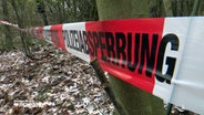 Flatterband mit dem Schriftzug "Polizeiabsperrung" hängt an mehreren Bäumen in einem Wald in Kaltenkirchen. © NDR 