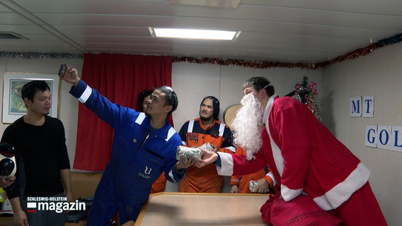 Seeleute machen ein Selfie mit einem als Weihnachtmann gekleideten Mann an Bord eines Schiffes in Brunsbüttel. © NDR 