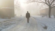 Eine Person läuft im winterlichen Nebel über einen Bauernhof. © NDR 