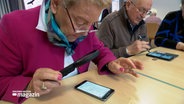 Senioren sitzen an einem Tisch und sind mit ihren Smartphones beschäftigt. © NDR 