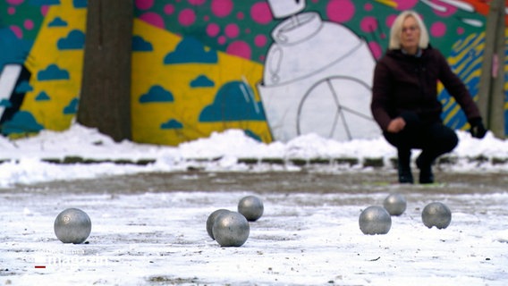 Eine Frau hockt auf einem Boul-Platz in Lübeck im Winter nach einem Wurf. © NDR 