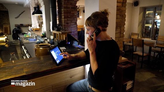 Eine Frau sitzt am Empfangstresen eines Restaurants in Flensburg und telefoniert. © NDR 