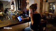 Eine Frau sitzt am Empfangstresen eines Restaurants in Flensburg und telefoniert. © NDR 