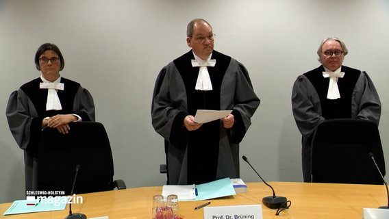 Drei Richter stehen in einem Gerichtssaal des Landesverfassungsgerichts in Schleswig bei einer Urteilsverkündung. © NDR 