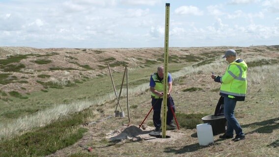 Mitarbeiter des Landesamts für Vermessung arbeiten an einem neuen Höhenmesspunkt nördlich von List in den Dünen auf Sylt © NDR Foto: NDR Screenshots