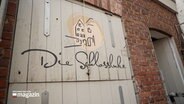 Eine Luke in einer Ziegelwand. Auf der Luke steht: "Die Schlossluke" © NDR Foto: NDR Screenshots