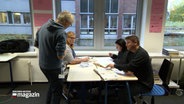 In einer Schule kommt ein lehrer an einen Tisch mit Schülern. © NDR Foto: NDR Screenshots