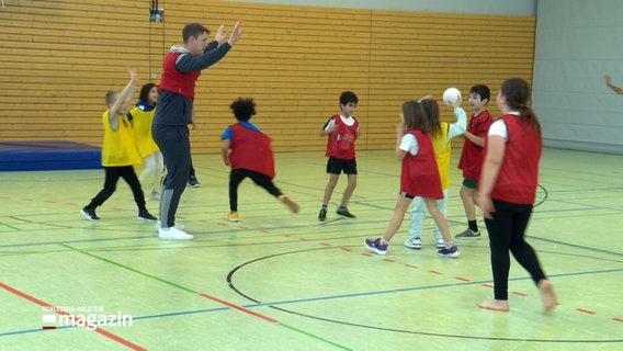 Ein Erwachsener spielt mit mehreren Kindern in einer Sporthalle Handball. © NDR Foto: NDR Screenshot