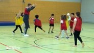 Ein Erwachsener spielt mit mehreren Kindern in einer Sporthalle Handball. © NDR Foto: NDR Screenshot