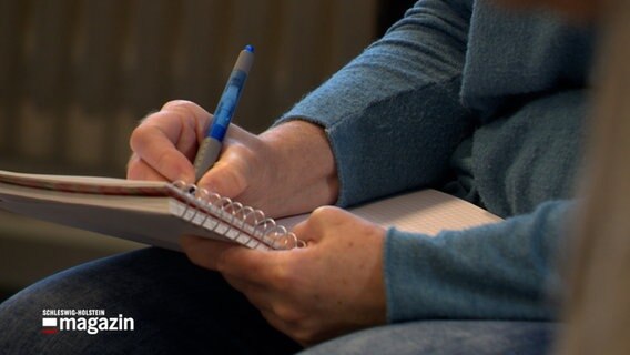 Eine Person schreibt auf einen Notizblock. © NDR Foto: NDR Screenshot