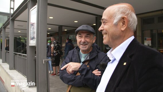 Giancarlo Orrù (links) und Orhan Aldemir (rechts) stehen am Eingang des Kieler Hauptbahnhofs und unterhalten sich © NDR Foto: NDR